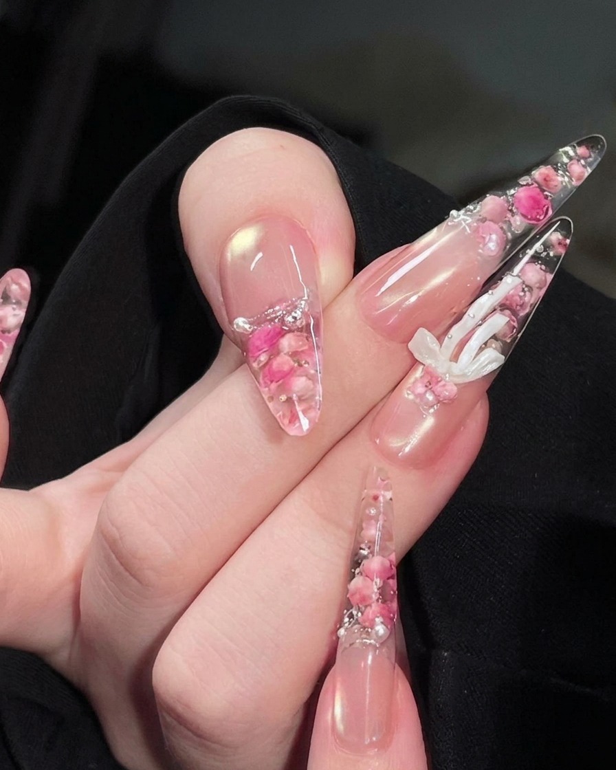 Una mano posicionada bajo una lámpara de uñas UV, con el diseño de rosas encapsuladas y perlas visible en las uñas.