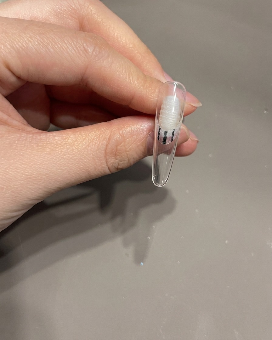 Primer plano de una mano colocando una uña con un lazo 3D bajo una lámpara de uñas UV para el curado.