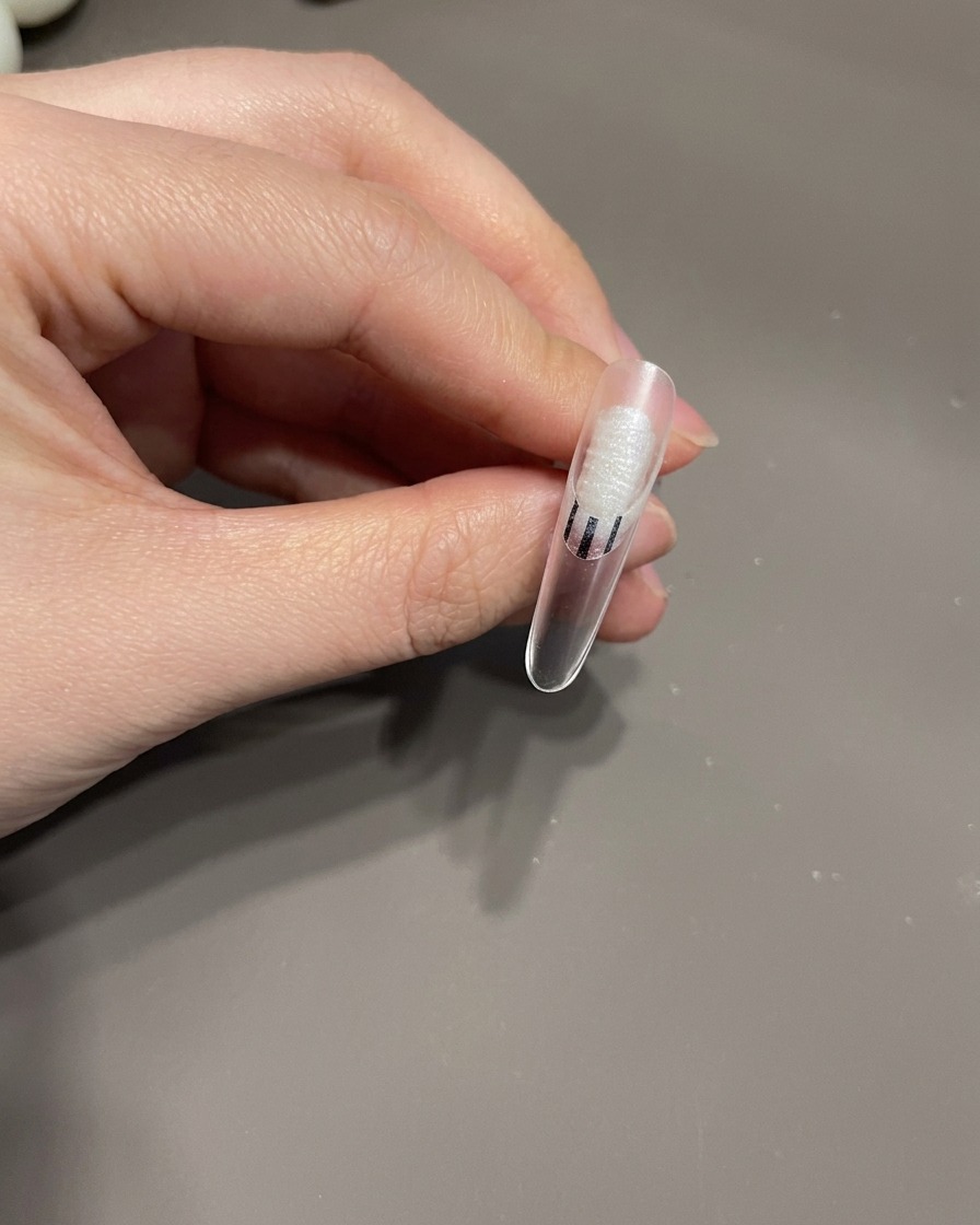 Un pincel de detalle dibujando finas líneas blancas en un patrón de espiral sobre una uña recubierta de gel.
