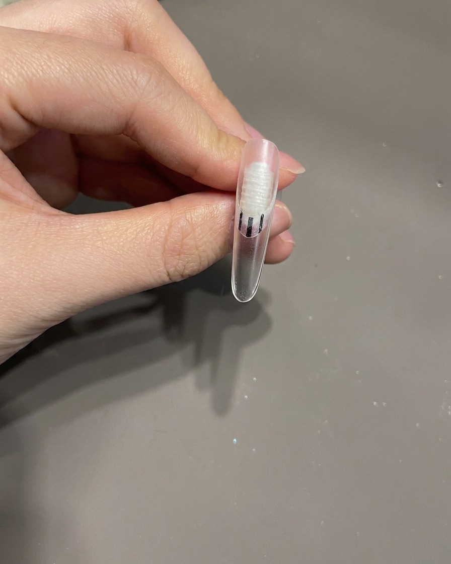 Un pincel de uñas aplicando una pequeña gota de top coat transparente sobre la superficie de la uña como pegamento para un adorno.