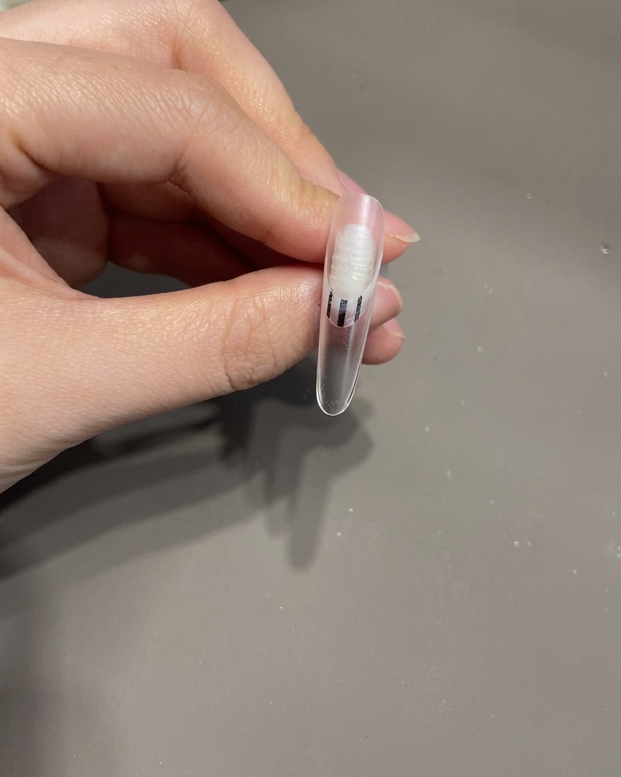 Pinzas colocando un pequeño lazo de gel 3D sobre la superficie de una uña manicurada.