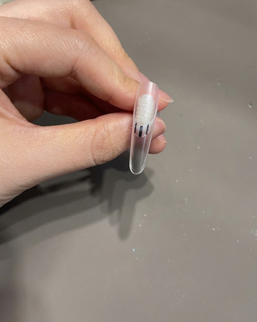 Una uña terminada con un lazo 3D y líneas blancas en espiral dentro de una lámpara UV para el proceso de curado final.