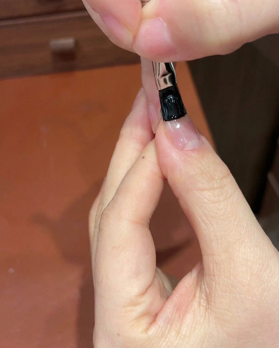 Primer plano de un pincel de detalle aplicando gel negro en el borde libre de la uña.