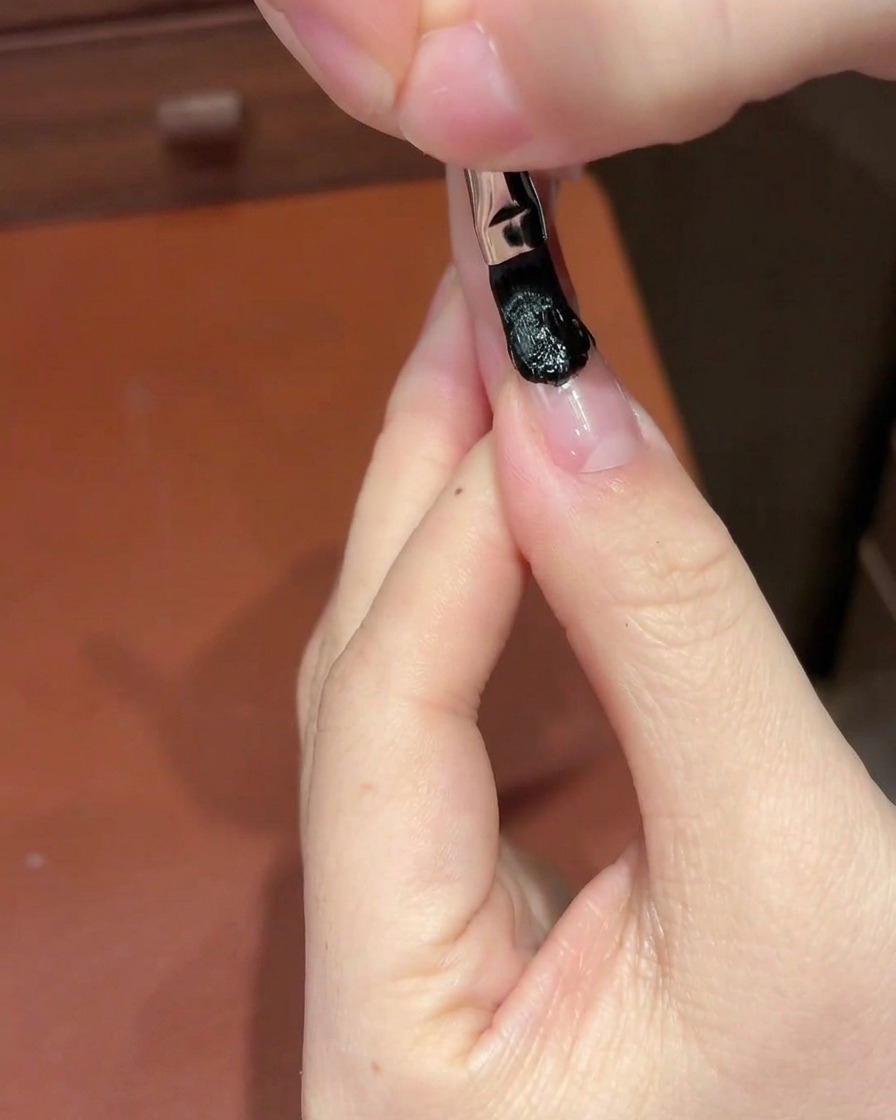 Una esponja cosmética blanca dando toques sobre la sección de gel negro en la uña para crear un degradado.