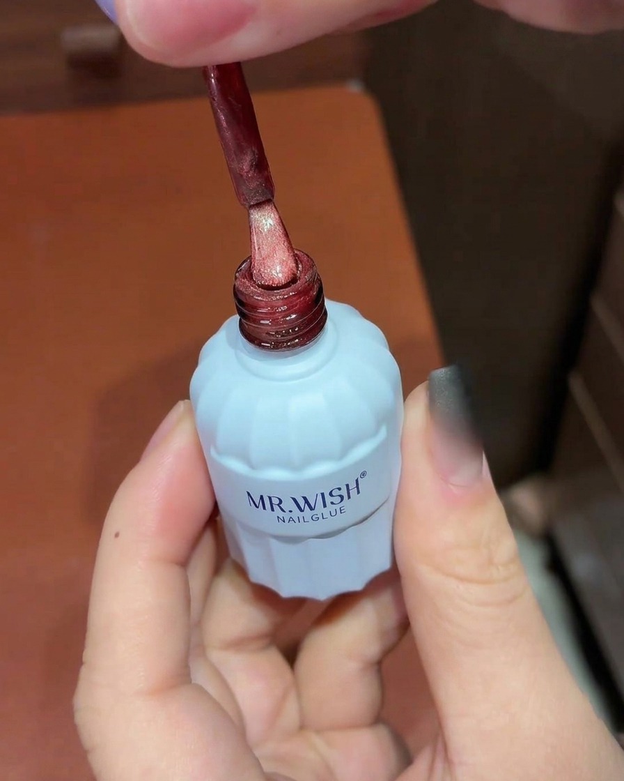 Un pincel aplicando esmalte de gel ojo de gato rojo brillante sobre una uña con ombré negro.
