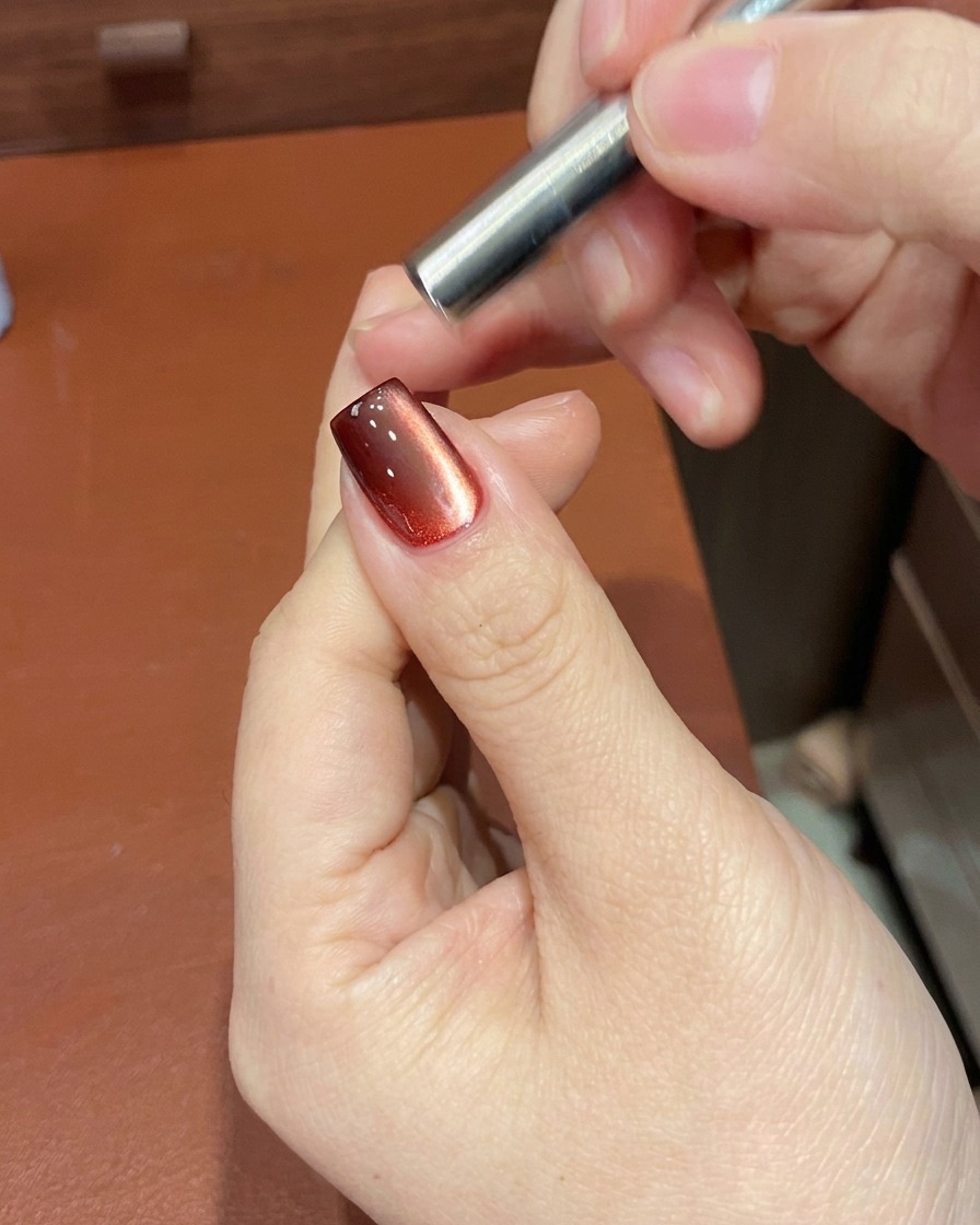 Una herramienta magnética posicionada cerca de la uña para manipular las partículas de brillo del esmalte de gel rojo.