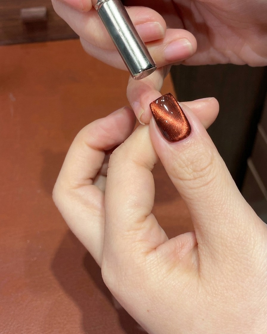 Primer plano de una uña de gel ojo de gato rojo con un imán cerca de la cutícula para desplazar el brillo magnético formando un degradado profundo.
