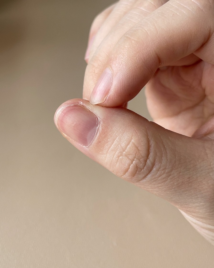 Primer plano de un lápiz de aceite para cutículas aplicándose en la piel que rodea una uña recién manicurada.