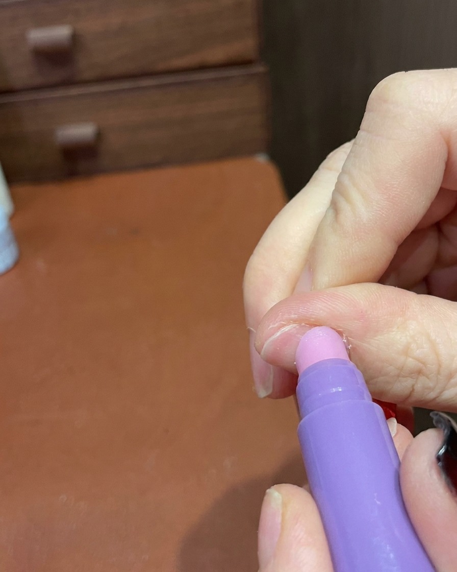 Primer plano de un lápiz de cuidado de cutículas utilizándose para suavizar suavemente la superficie y los bordes de una manicura terminada.