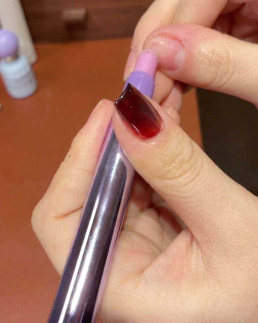 Una mano usando una toallita sin pelusa para limpiar la piel y los bordes alrededor de una uña terminada con manicura de gel.
