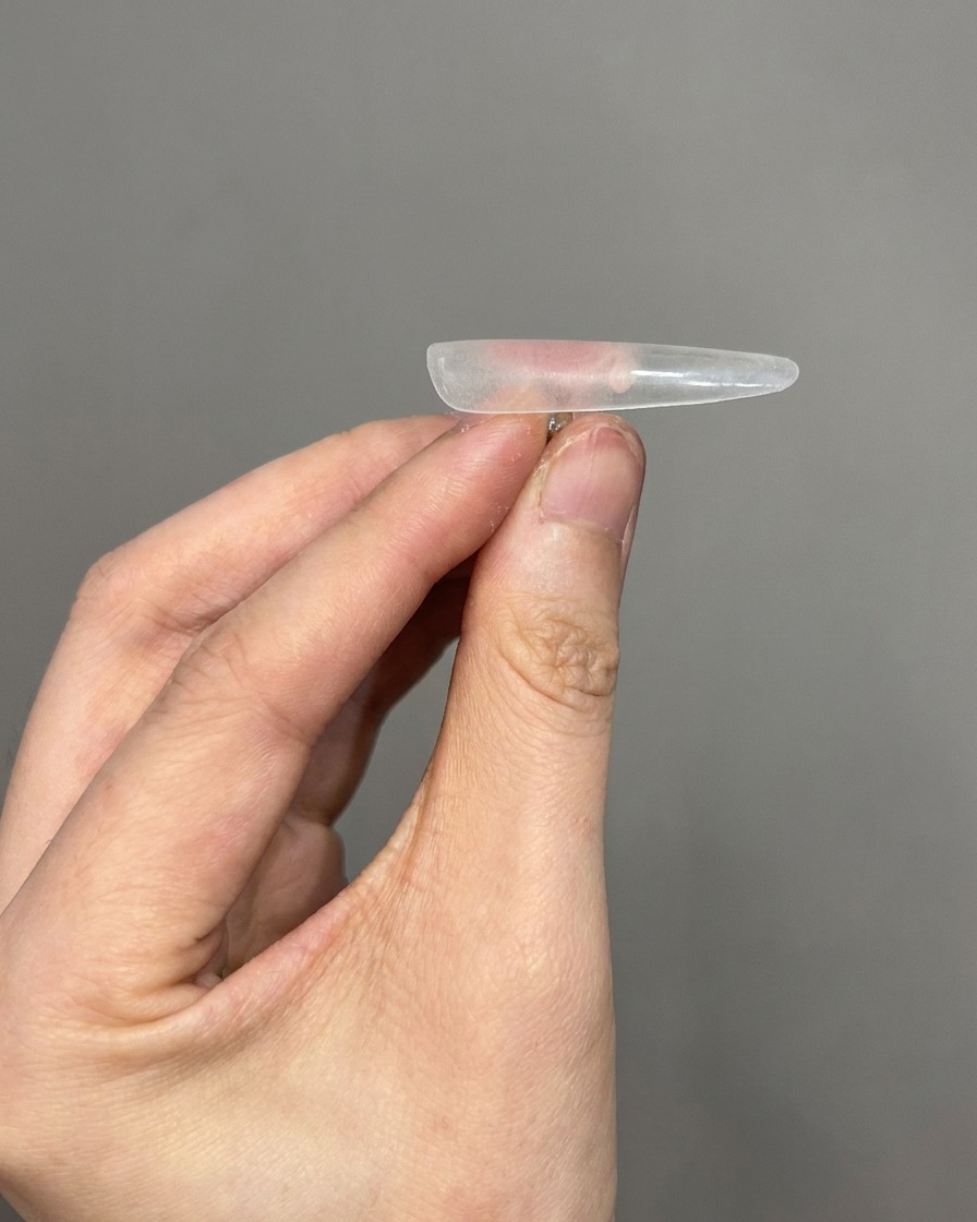 Vista en primer plano de un cepillo eliminando el polvo fino de la superficie de una uña postiza transparente.