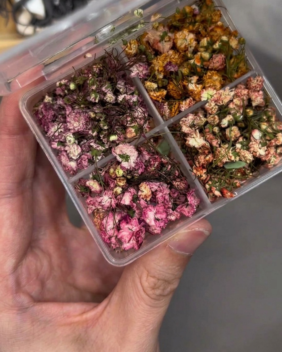 Pinzas colocando con precisión una pequeña flor seca sobre la superficie de la uña.