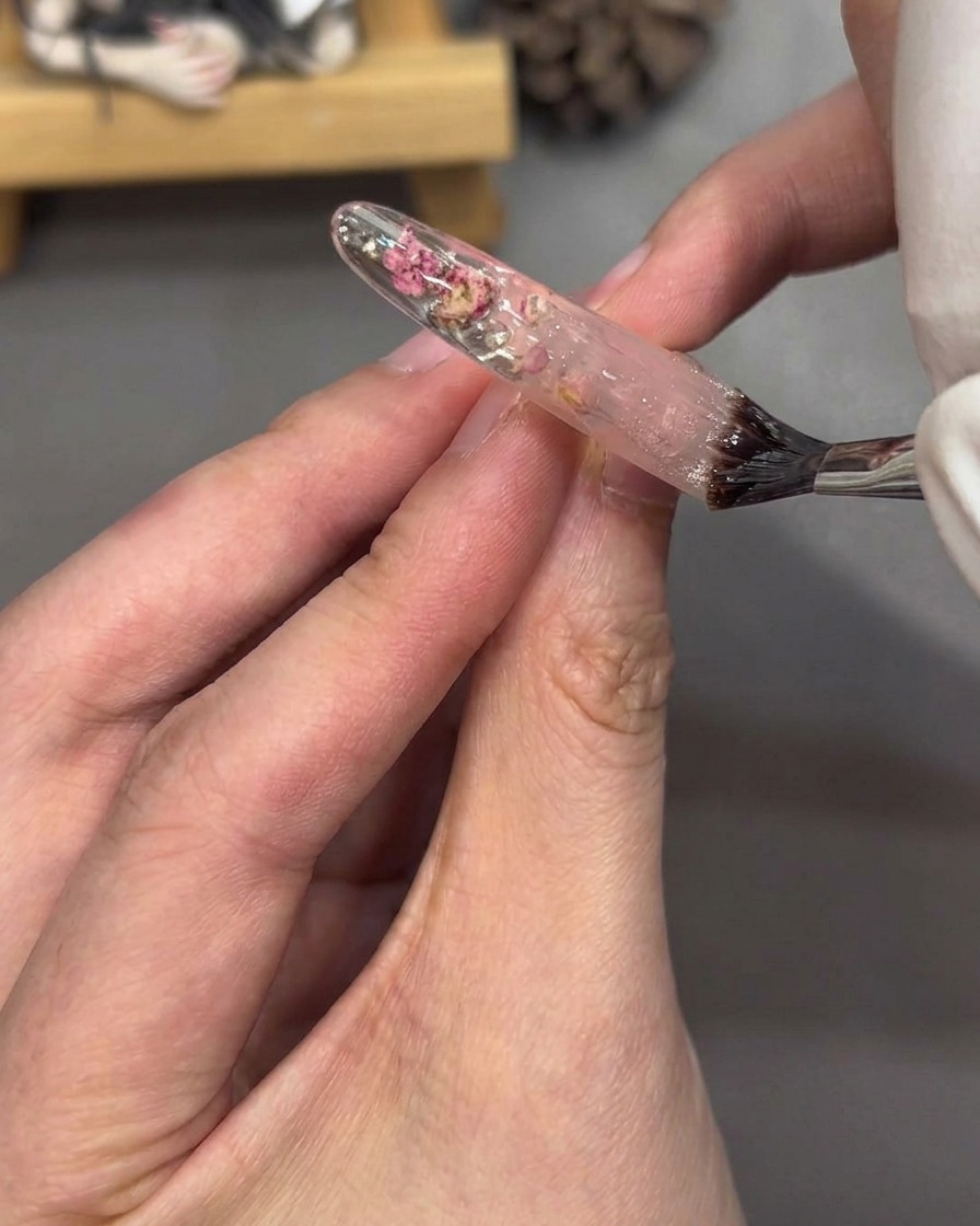 Un pincel aplicando top coat transparente sobre la uña decorada, creando un acabado brillante.