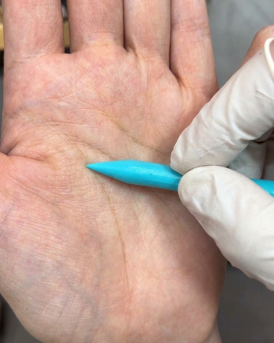 Una herramienta de escultura presionando una perla de gel blanco sobre una superficie, formando un pétalo delicado.