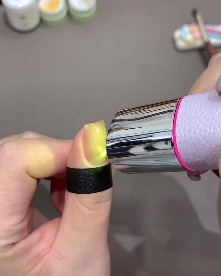 Una uña brillando bajo una lámpara UV/LED portátil para curar el esmalte.