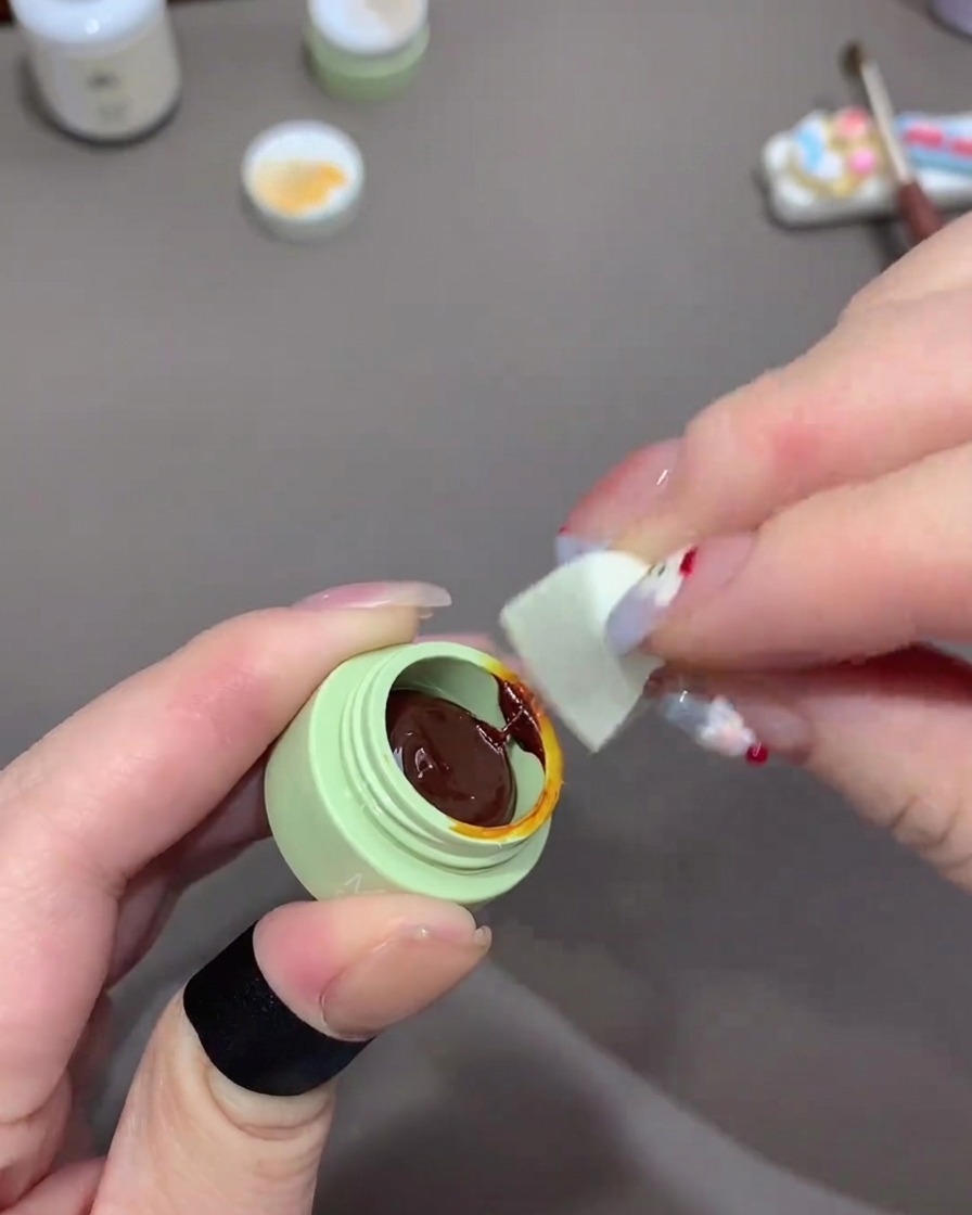 Una mano usando un trozo pequeño de esponja de maquillaje para recoger gel naranja.