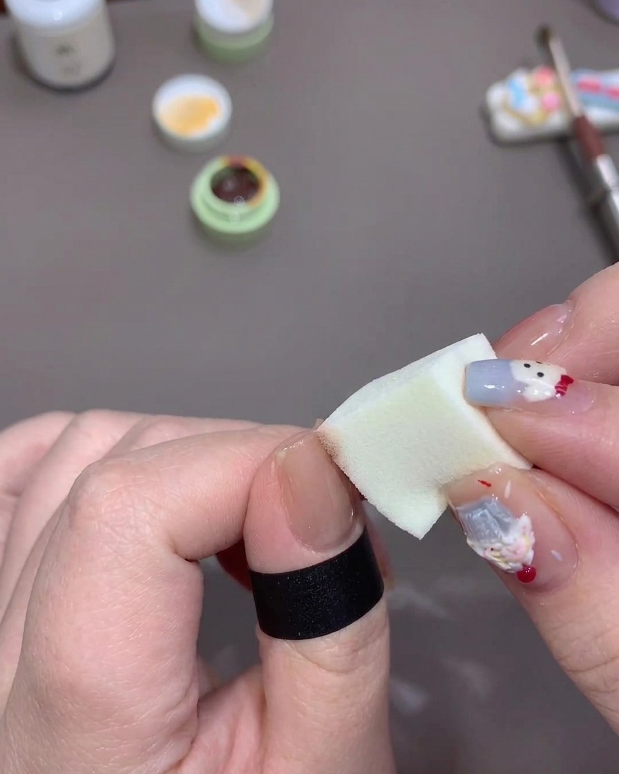 Una mano aplicando gel naranja sobre la punta de una uña con una esponja para crear un desvanecido.