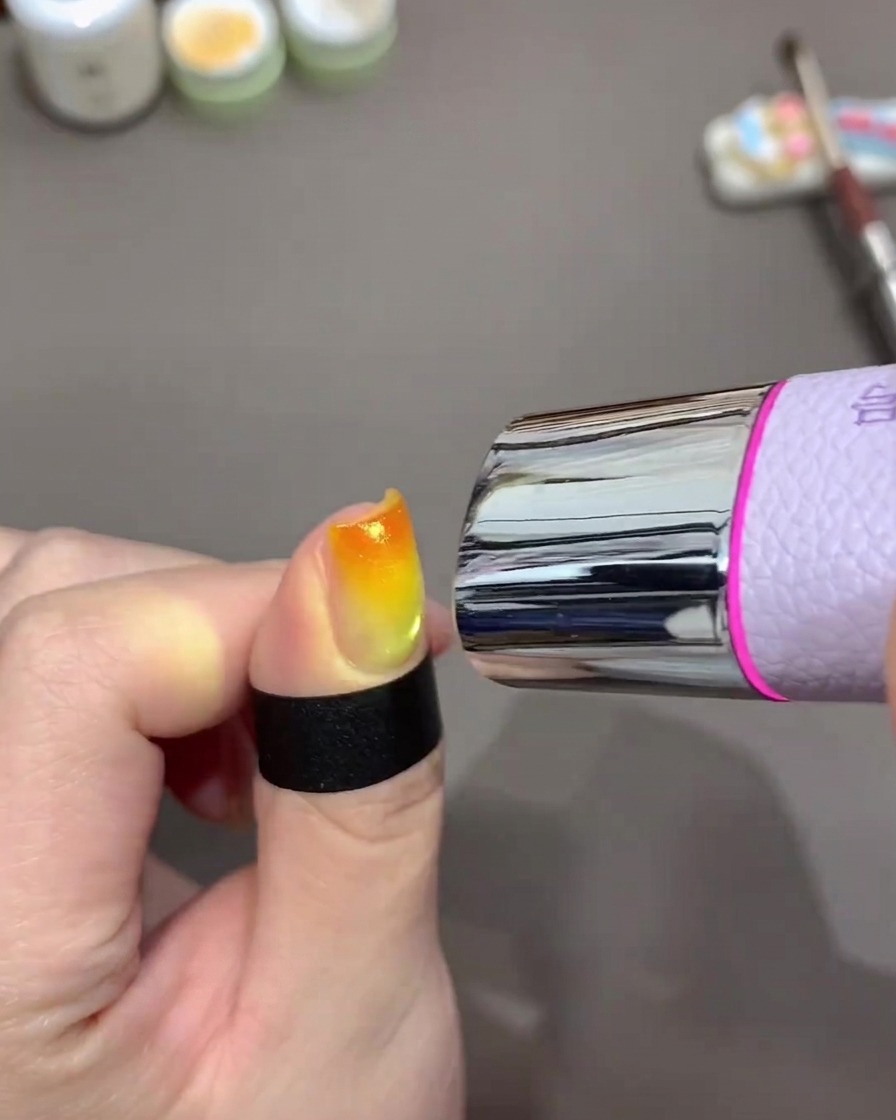 Una mini lámpara UV sobre la uña curando el diseño degradado.