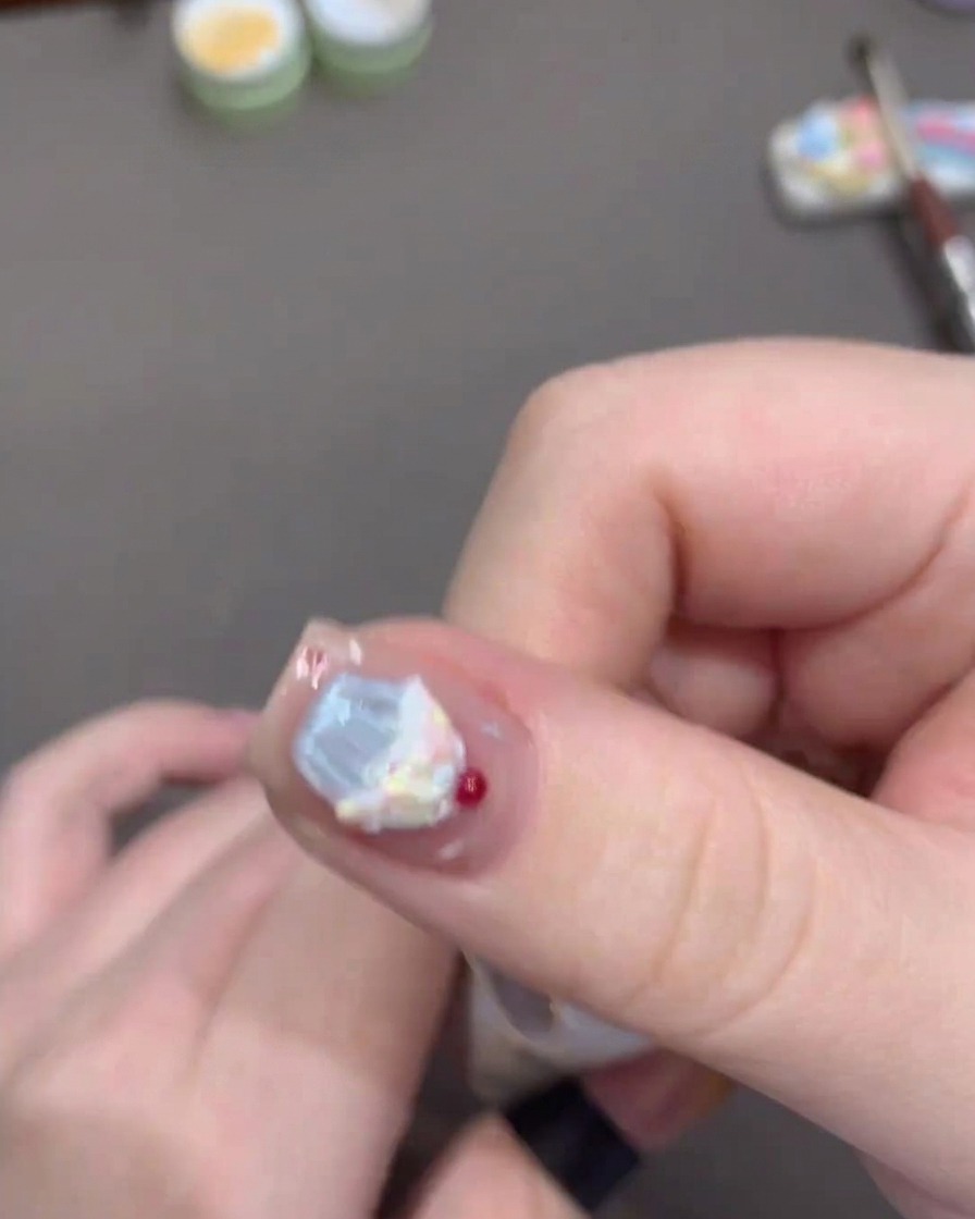 Un pincel aplicando top coat brillante sobre el diseño de uñas.