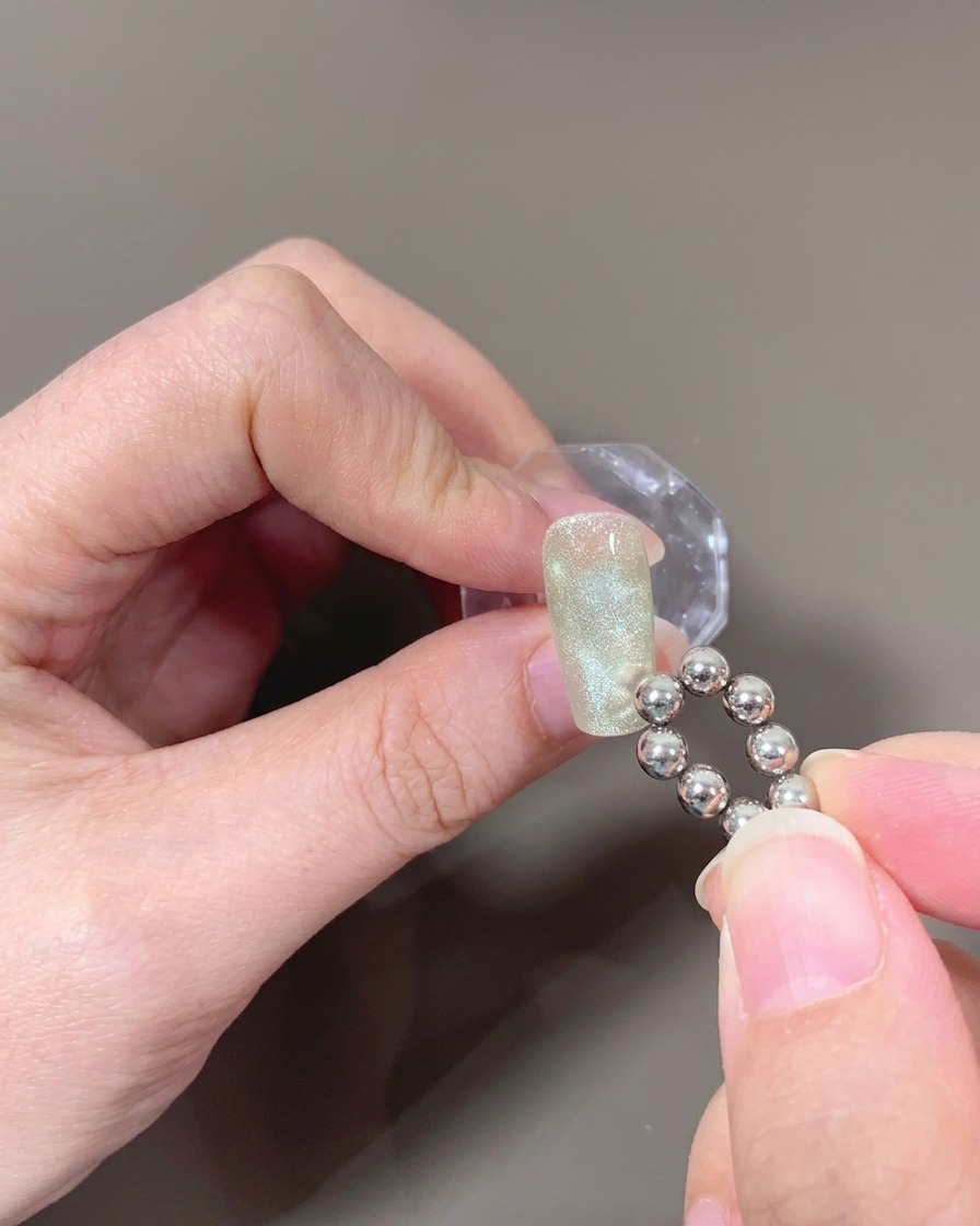 Un primer plano de una uña con gel ojo de gato sin curar, con un imán de punta esférica creando un patrón de ondas.
