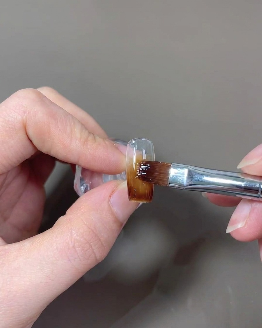 Un pincel aplicando una capa final de top coat brillante a la uña.
