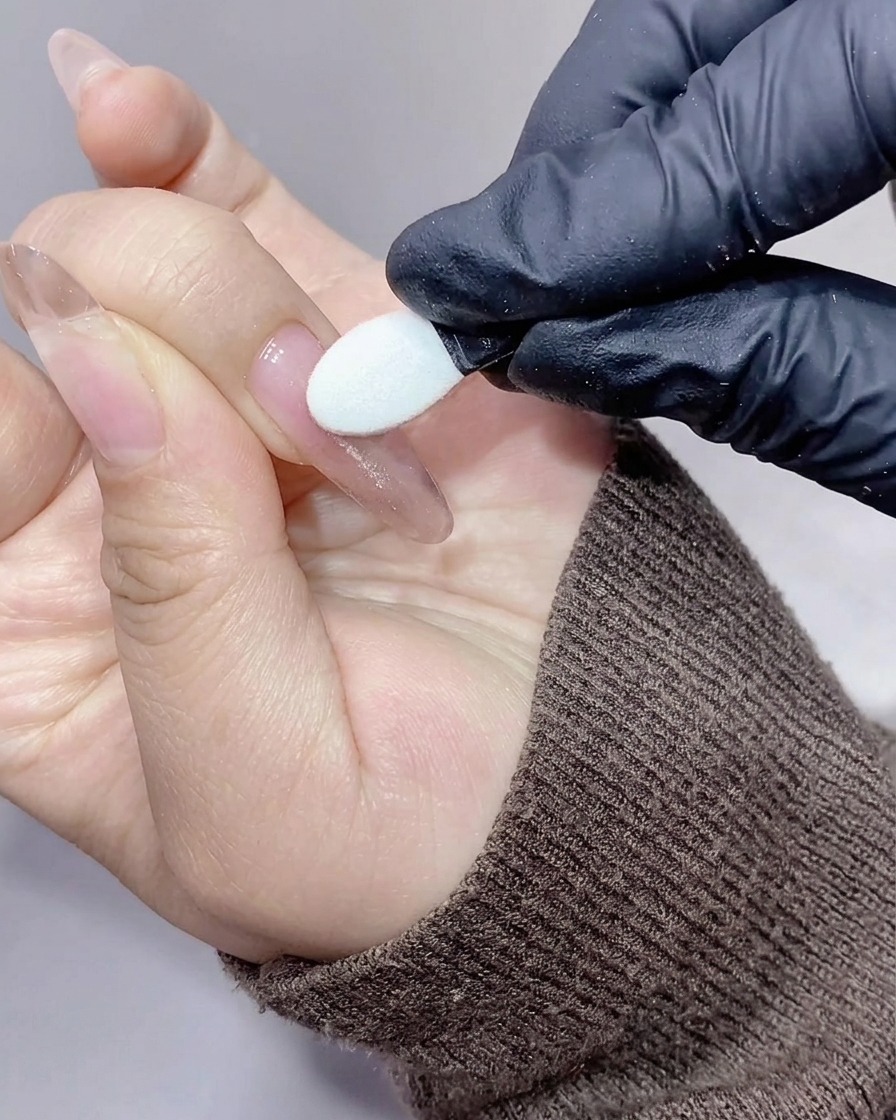 Un aplicador de silicona frotando polvo de cromo aurora iridiscente y brillante sobre la superficie de una uña.