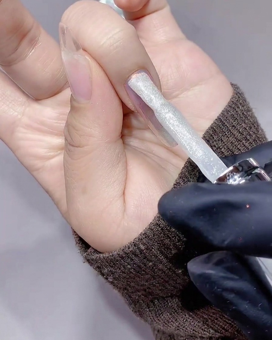 Un pincel aplicando una capa de gel de diamante triturado brillante y plateado sobre una uña.