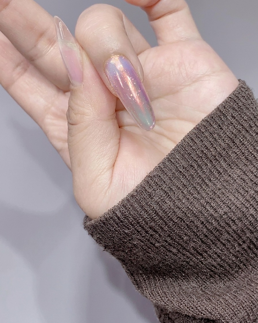 Las uñas siendo curadas bajo una pequeña lámpara UV/LED rosa después de la aplicación de gel de brillantina plateada.