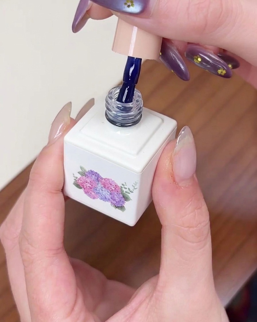 Un pincel aplicando esmalte de gel azul oscuro sobre una uña preparada, asegurando una cobertura uniforme.