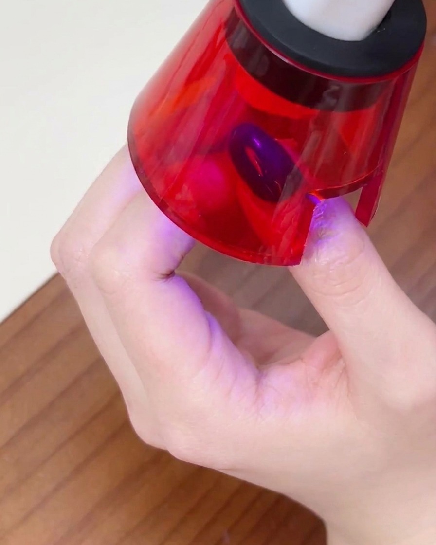 Una mano posicionada dentro de una lámpara de uñas UV pequeña, con el dedo centrado para curar el esmalte.