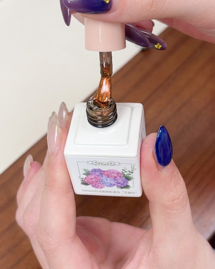 Un pincel aplicando una capa de gel magnético cat eye color ámbar transparente sobre la base azul oscura.