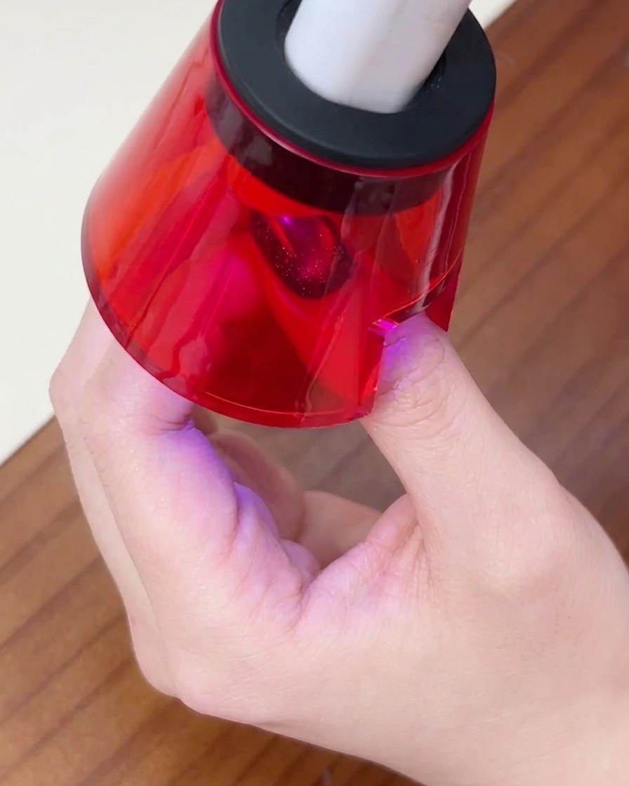 El dedo de una persona descansando bajo una pequeña lámpara de uñas UV/LED roja para curar la capa final de gel.