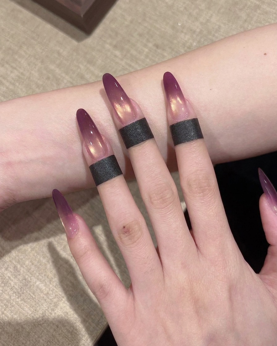 Primer plano de una pequeña esponja dando ligeros toques para difuminar el gel morado en una extensión de uña creando un efecto ombré.