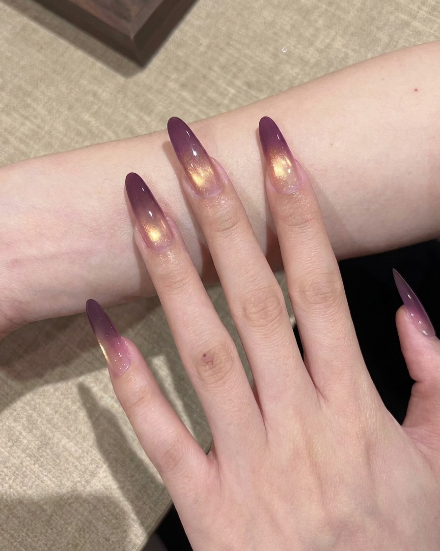 Una mano con uñas en degradado morado y dorado colocada dentro de una lámpara UV profesional para su curado.