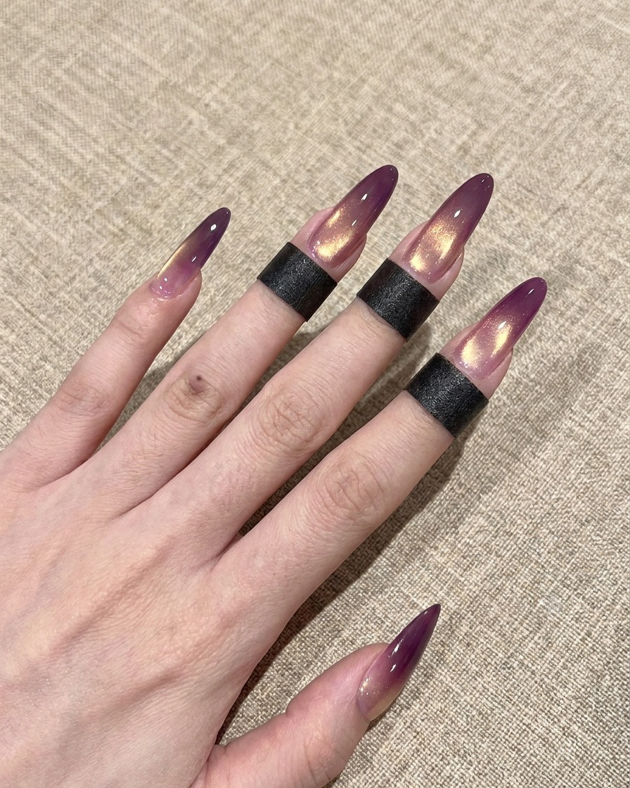 Primer plano de un pincel aplicando una capa superior transparente y brillante sobre una uña ojo de gato con degradado morado y dorado.