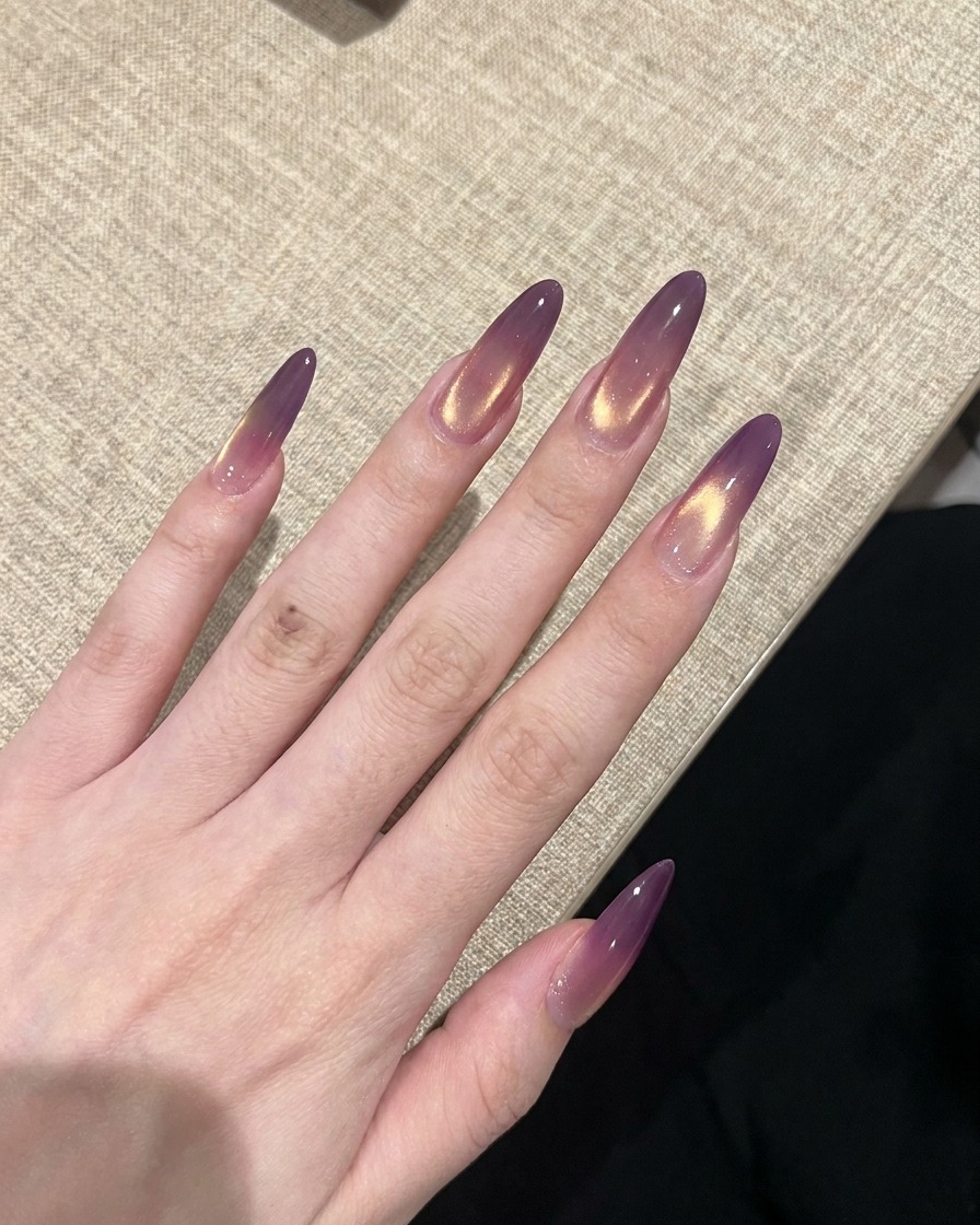Una mano con el diseño de uñas ojo de gato en degradado morado y dorado terminado curándose bajo una lámpara UV.