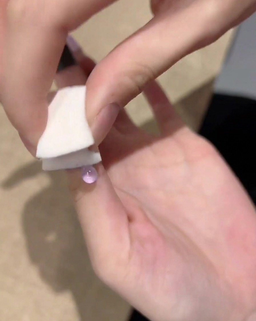 Una mano usando una pequeña esponja blanca para dar toques y difuminar el esmalte de gel morado desde la punta de la uña hacia el centro.