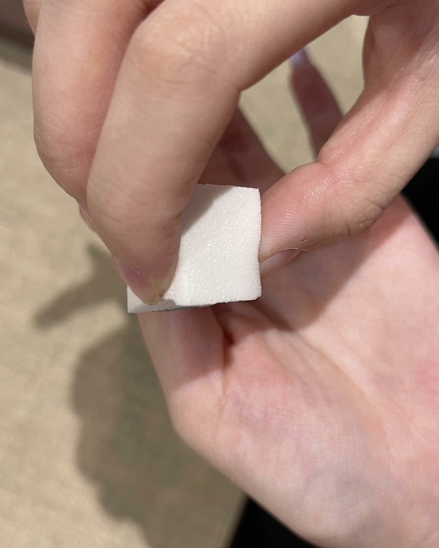 Una esponja de maquillaje blanca aplicando un esmalte de gel morado oscuro en el borde libre de una uña.