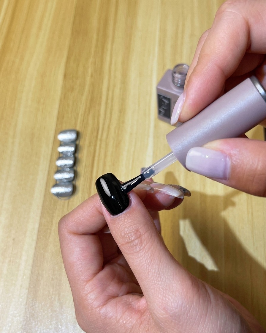 Aplicando una capa transparente de top coat sin residuo sobre la uña de gel negro curado.