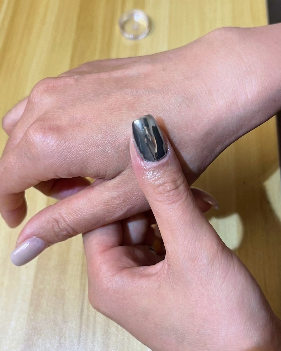 Un aplicador de esponja frotando pigmento de cromo plateado sobre una uña pintada con gel negro.