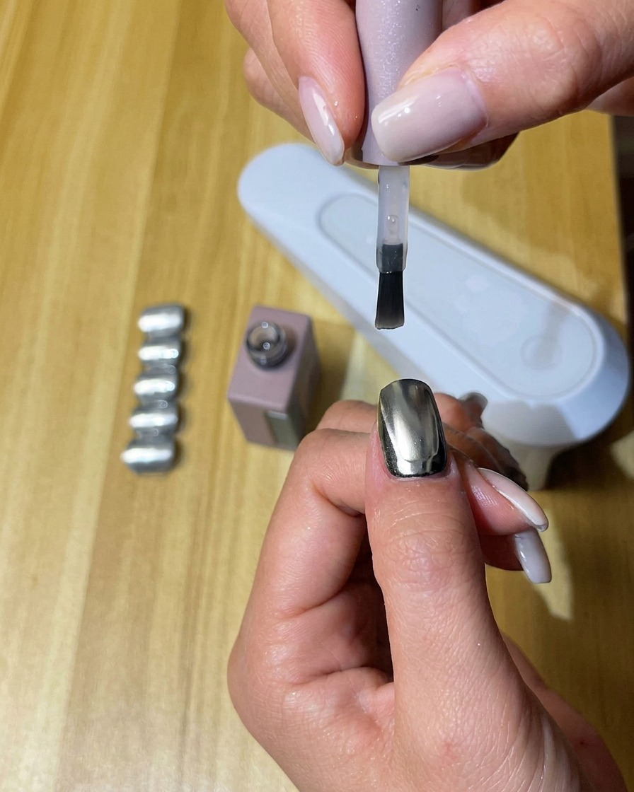 Una mano con uñas recubiertas de top coat mate curándose dentro de una lámpara de uñas UV/LED.