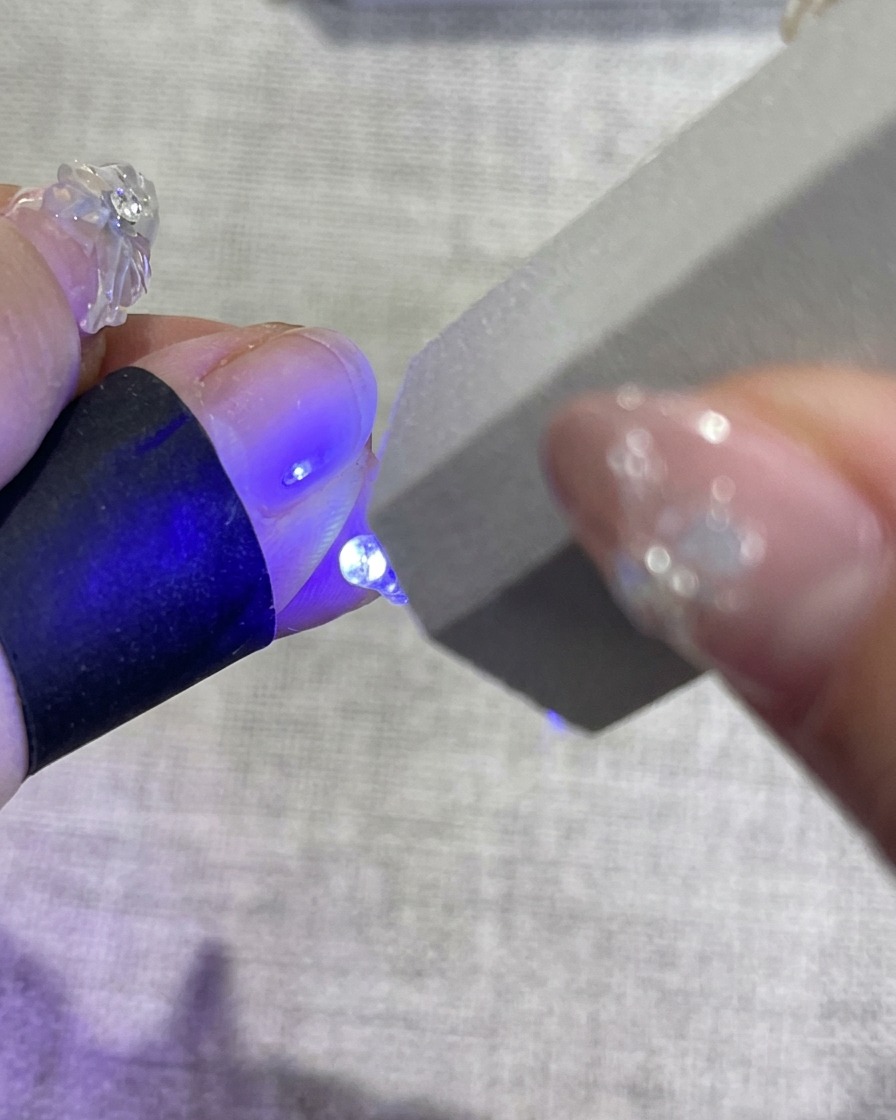 Una mano con uñas florales decoradas dentro de una lámpara UV, con luz azul emitiéndose para curar el esmalte.