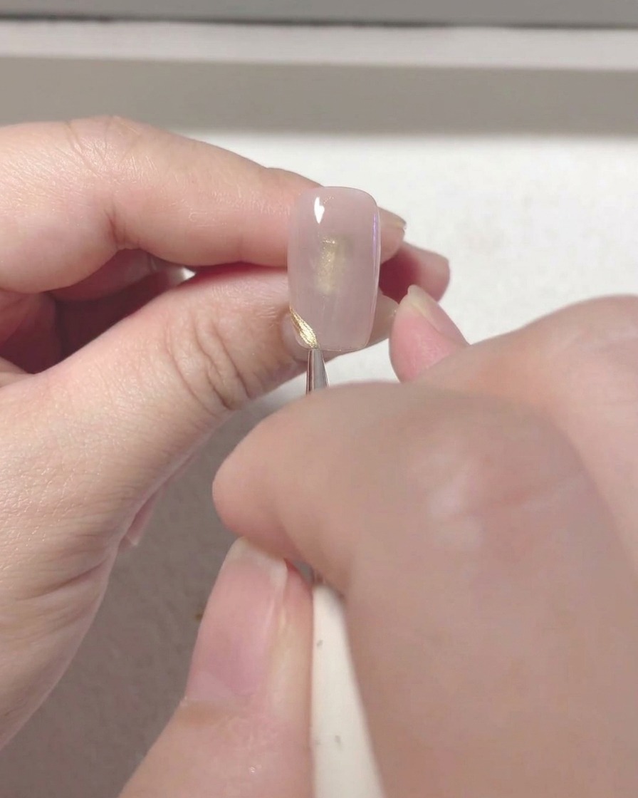 Un pincel fino para nail art dibujando una línea roja y precisa para la punta francesa en el borde de una uña.