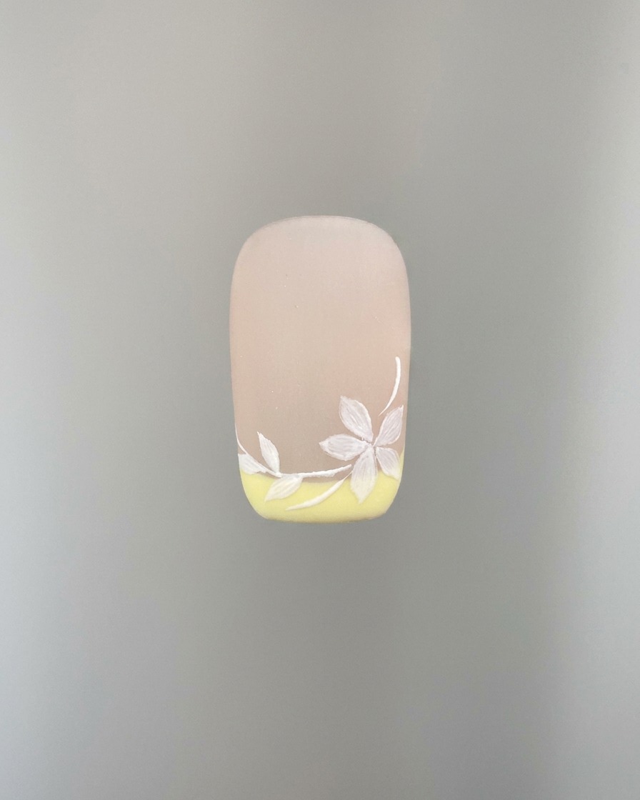 Una foto detallada que muestra cómo se añaden más pétalos de flor de sakura blancos al diseño de la uña.