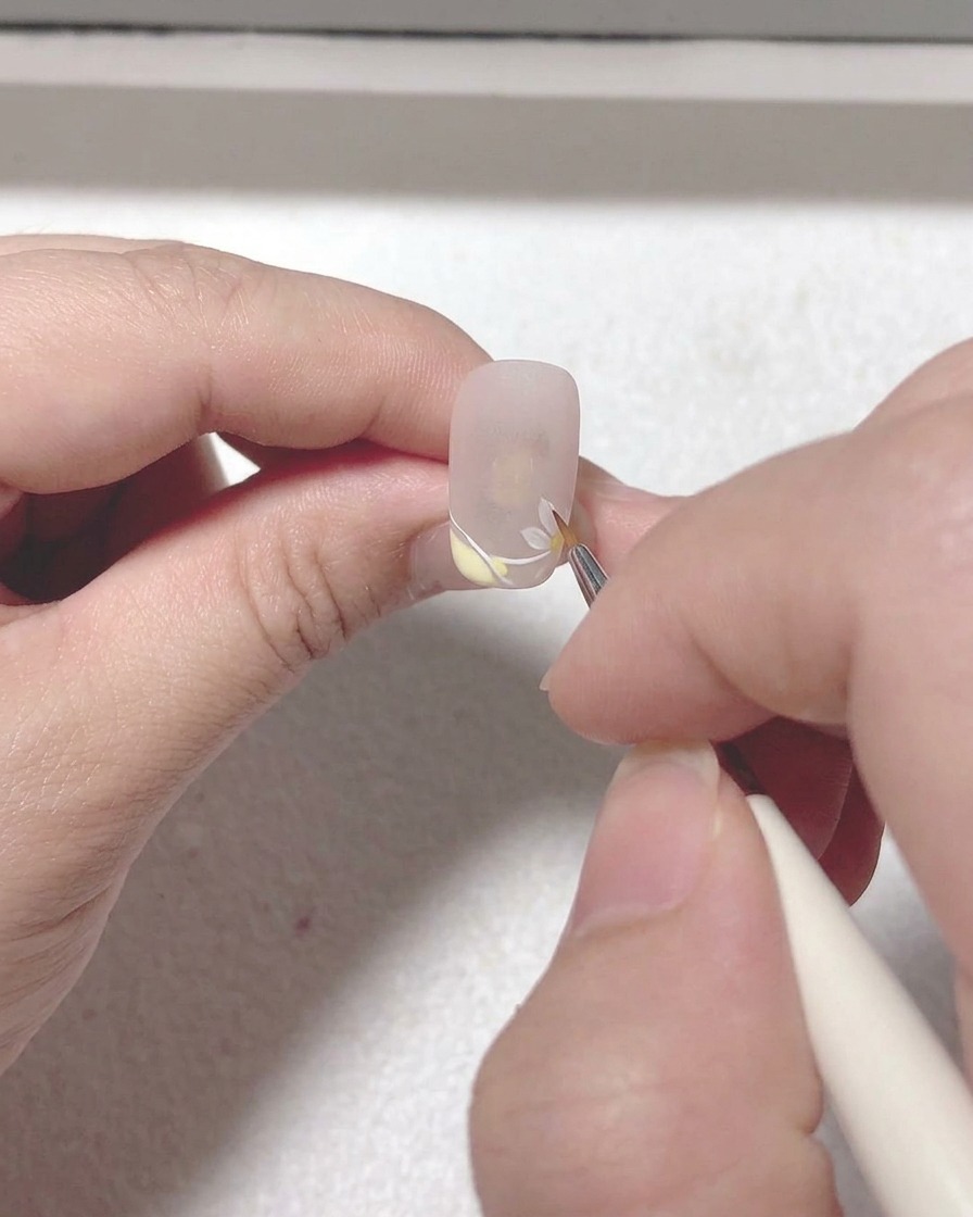 Un pincel liner muy fino añadiendo detalles de ramas finas e intrincadas y hojas junto a la flor de sakura pintada.