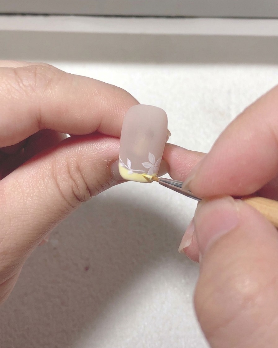 Un primer plano de un pincel liner añadiendo toques finales y perfeccionando las líneas en el diseño de nail art de sakura.