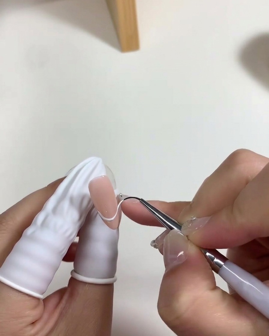 Un pincel aplicando una capa fina de esmalte de gel blanco lechoso sobre la base de la uña.
