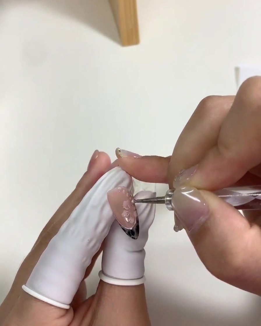 Primer plano de una herramienta de puntos colocando pequeños puntos blancos alrededor de las flores de cerezo.