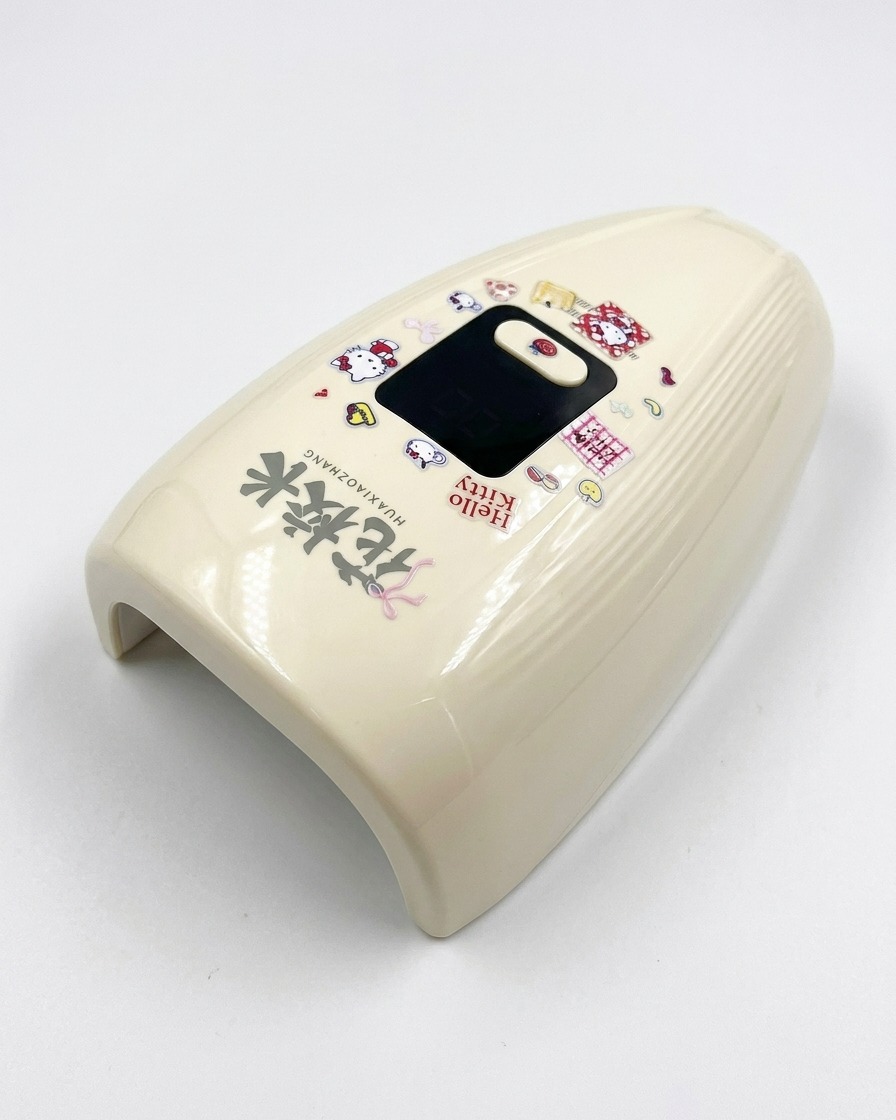 Una lámpara UV/LED mini de color crema decorada con pegatinas de Hello Kitty sobre una superficie blanca.
