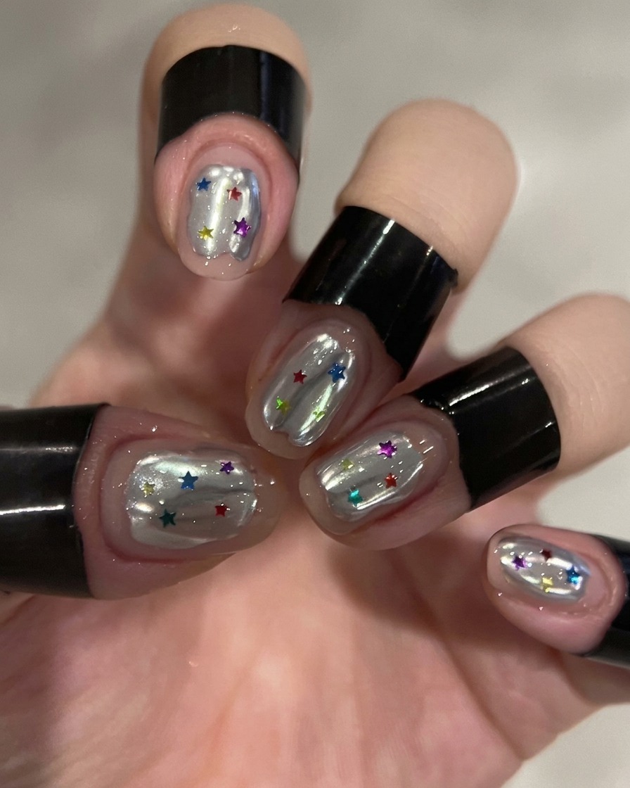Una mano con uñas cromadas plateadas decoradas con estrellas coloridas descansando dentro de una lámpara de uñas UV/LED profesional.